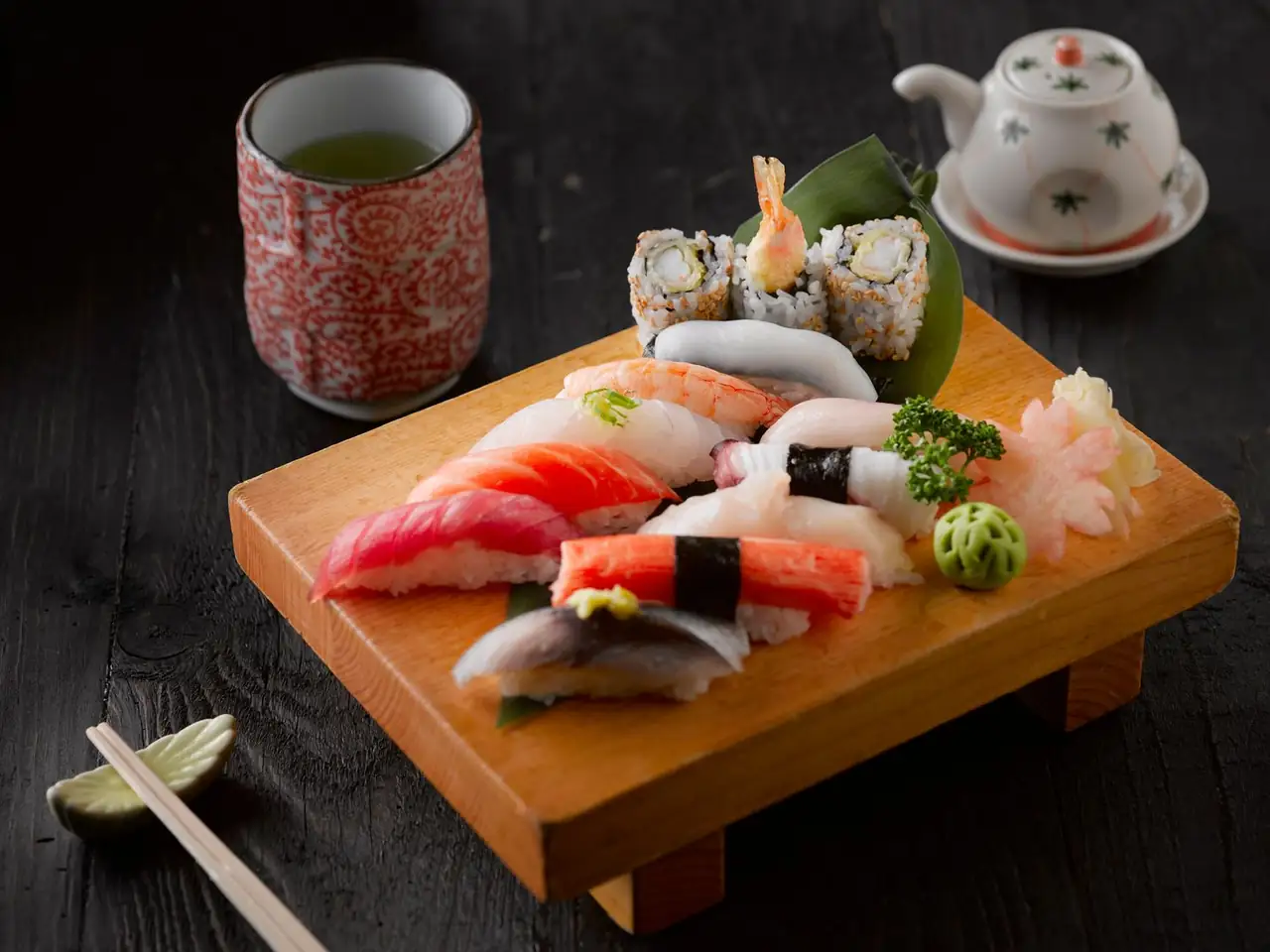 Chef preparing delicate sushi rolls and nigiri with freshly poured green tea