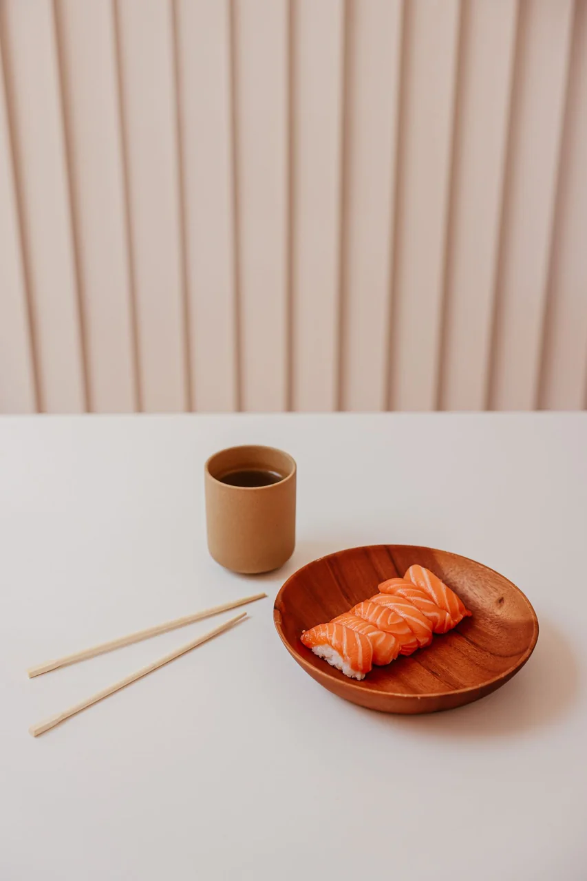 Minimalist presentation of salmon nigiri sushi on artisanal ceramic plate with warm wooden backdrop