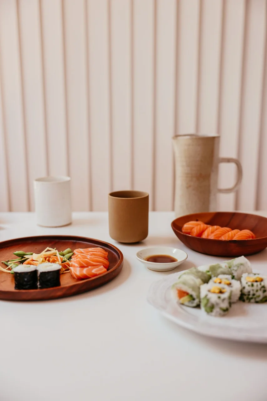 Salmon nigiri and maki rolls with ceramic shoyu vessel on dark timber