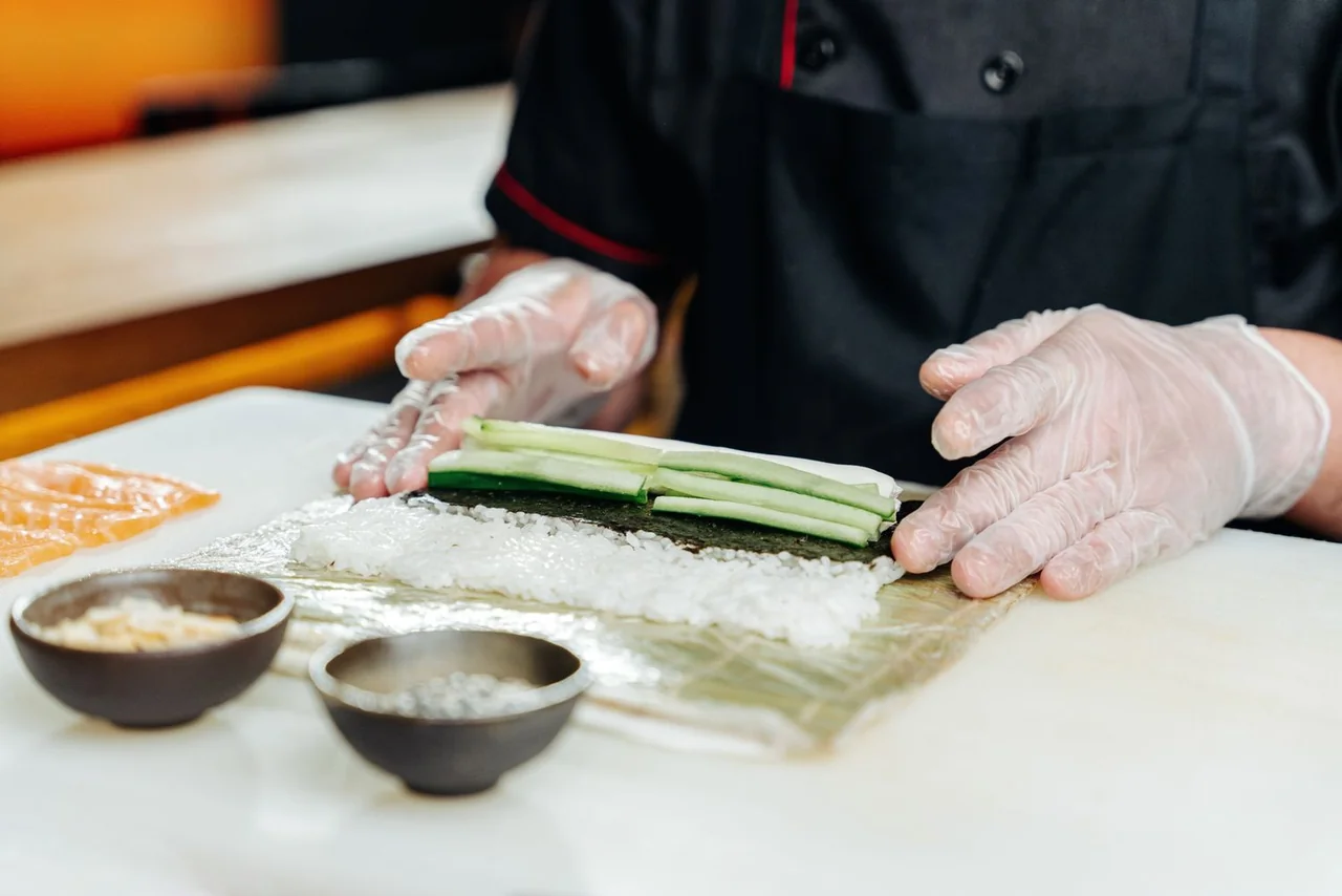 Chef preparing sushi roll with exact hand positioning and fresh ingredients